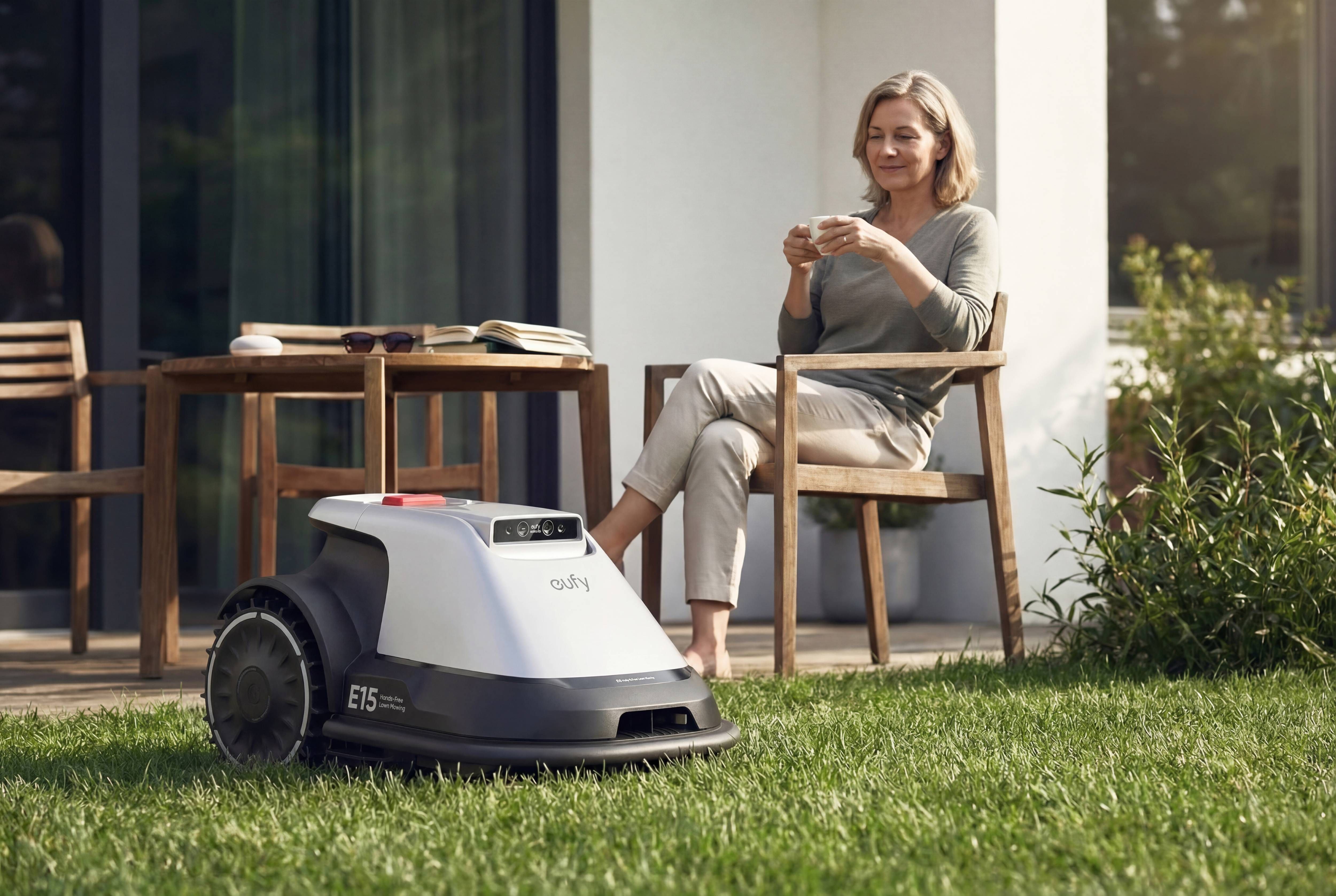 Eufy E15 Mähroboter mäht selbstständig den Rasen vor einer Terrasse, während eine Frau entspannt im Garten sitzt